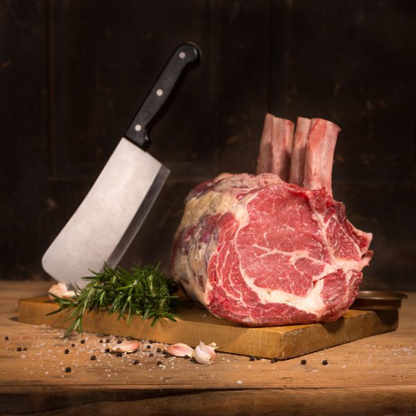 Raw rib eye roast on cutting board with meat clever and spices.